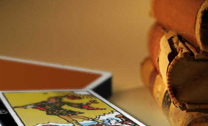 Close-up view of a stack of old books, along with a view of The Fool card from Tarot.