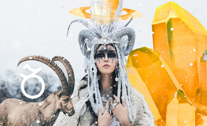 A woman with a horned headdress and dark makeup stands in the snow beside a goat.